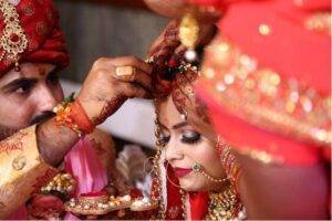 Asian Bride on her wedding day. She is wearing traditional bridal makeup and the groom is adjusting her teeka